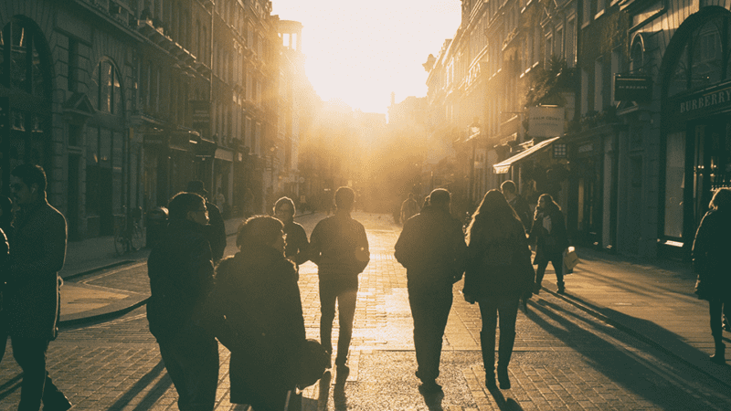 Pedestrians walk a busy street with the morning sun shining