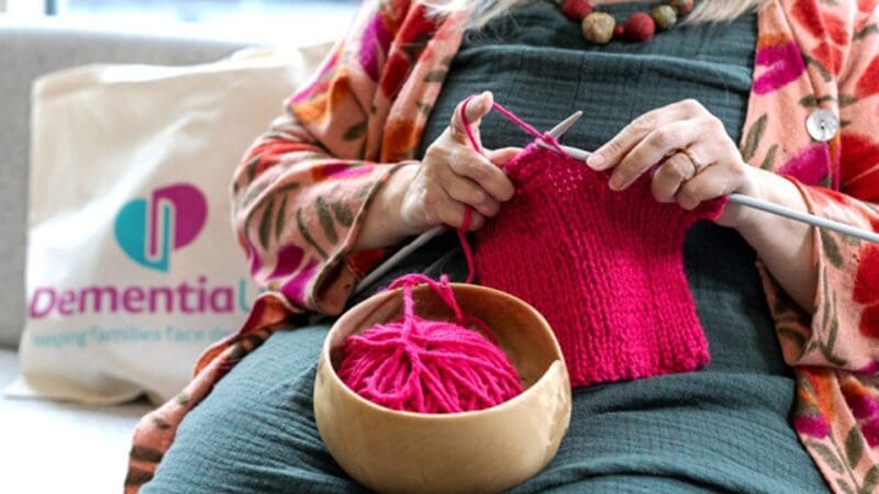 person knitting with a dementia uk tote bag next to them